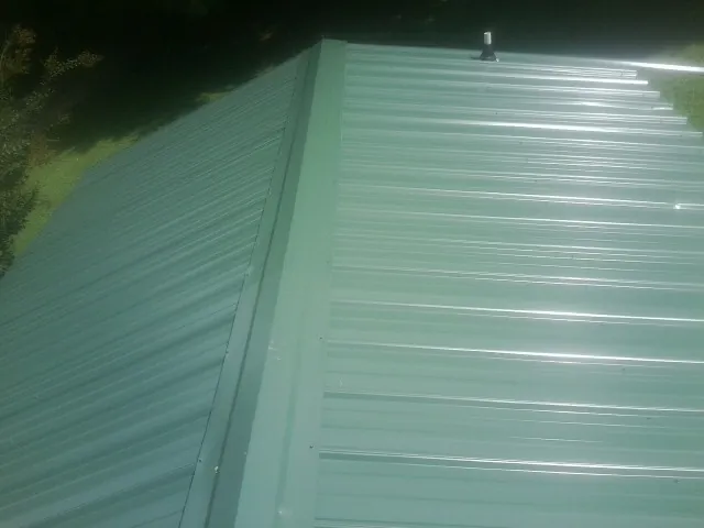 New green metal panels meeting at the ridge of a roof — Flat Roof Repair work by our crew in Blackshear