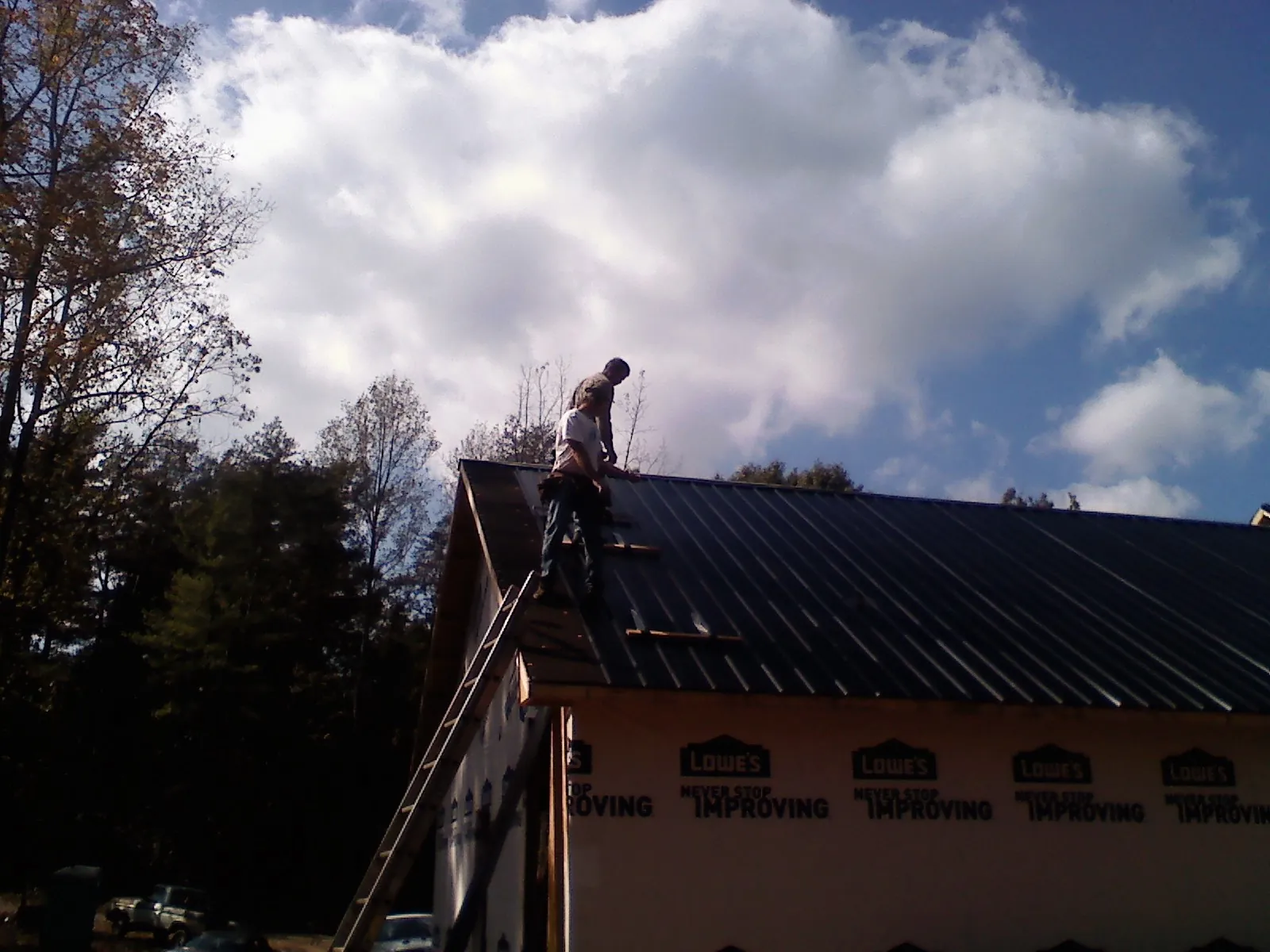 Roofer fastening dark metal panels high against a cloudy sky, from a Roof Inspection job in Blackshear