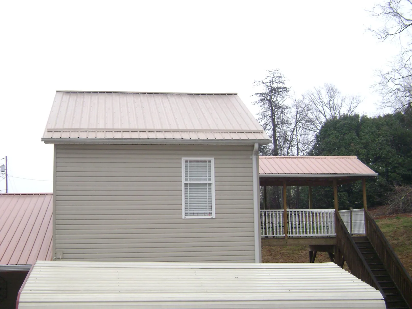 Tan metal roofs on a two story addition and attached porch, from a Roof Replacement job in Blackshear